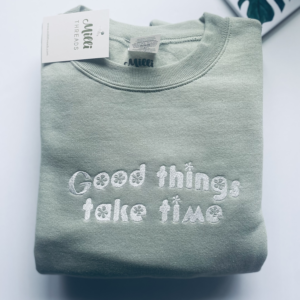 Embroidered Good things take time white treads on the sage green sweatshirt.